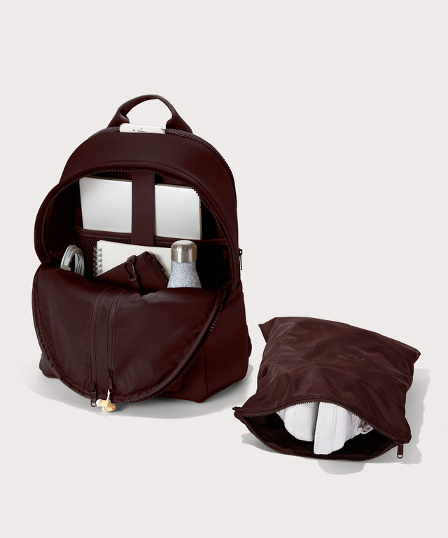 Dagne Dover Large Dakota Neoprene Backpack in a deep brown with purple undertones unzipped, showing the interior pockets and shoe bag.