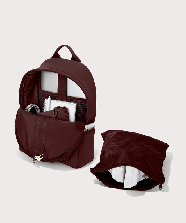 Dagne Dover Medium Dakota Neoprene Backpack in a deep brown with purple undertones unzipped, showing the interior pockets and shoe bag.