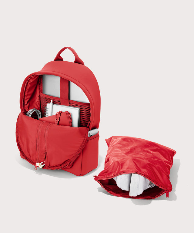 Dagne Dover Medium Dakota Backpack in a fiery, saturated red leaning toward orange unzipped, showing the interior pockets and shoe bag.