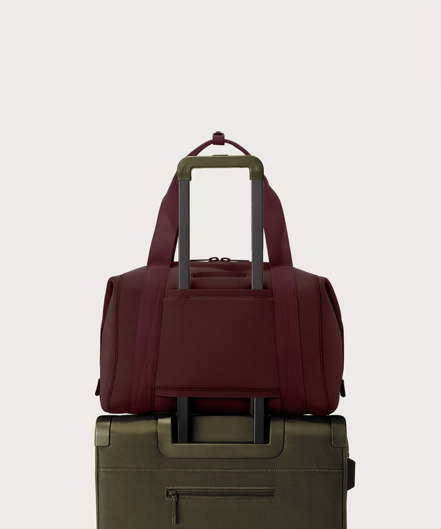 Maroon duffel bag on top of a green suitcase on a light beige background