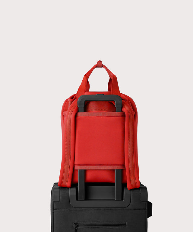 Dagne Dover Rhys Backpack in a fiery, saturated red leaning toward orange on luggage, showing the luggage sleeve.