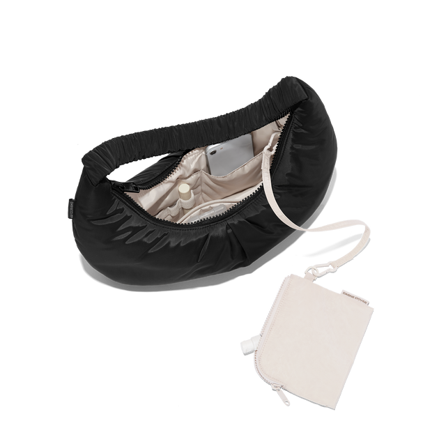 hover - Dagne Dover Rider Shoulder Bag in black unzipped, revealing the interior elastic loops, interior zip pocket, and removable zippered pouch.