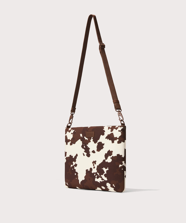 14 inch laptop shoulder bag in a cow print seen from the angle view. 
