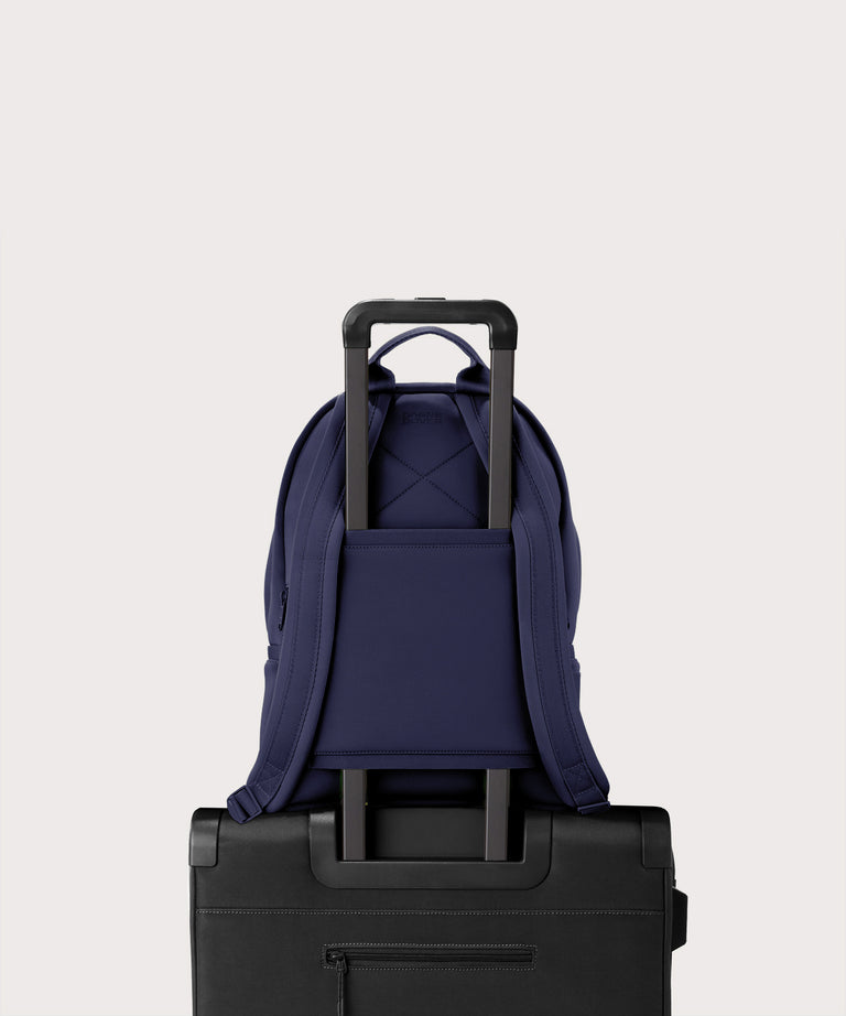 Dagne Dover medium Dakota Neoprene Backpack in dark blue strapped to luggage with the neoprene luggage-handle sleeve.
