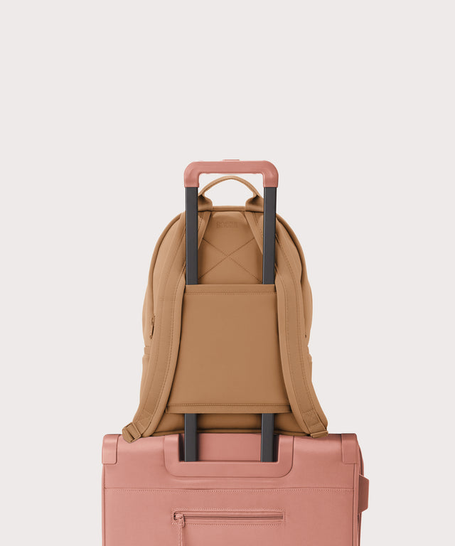 Dagne Dover medium Dakota Neoprene Backpack in camel brown strapped to luggage with the neoprene luggage-handle sleeve.