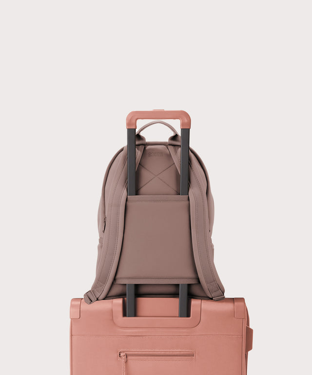 Dagne Dover medium Dakota Neoprene Backpack in pink strapped to luggage with the neoprene luggage-handle sleeve.
