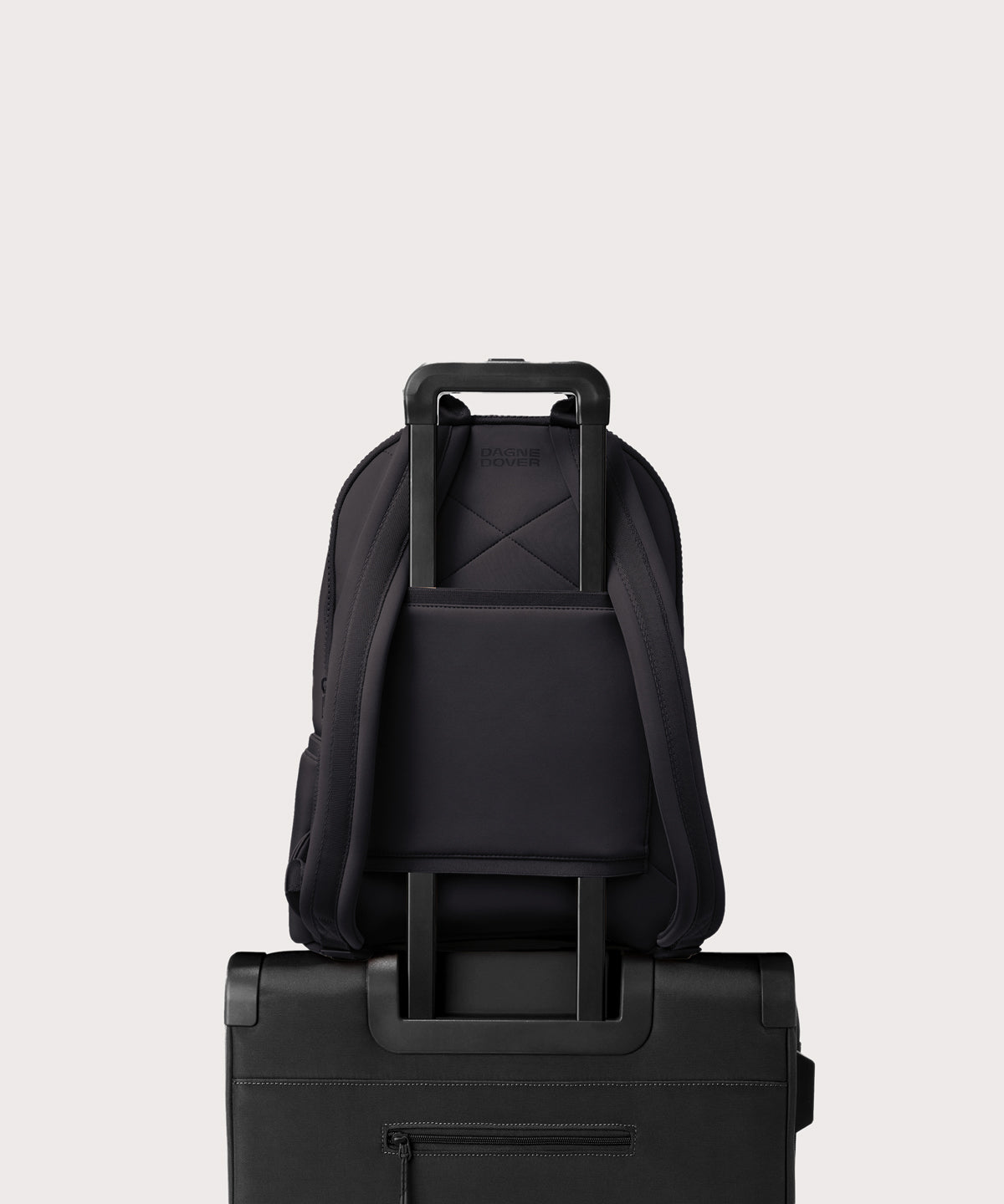 Dagne Dover large Dakota Neoprene Backpack in black strapped to luggage with the neoprene luggage-handle sleeve.
