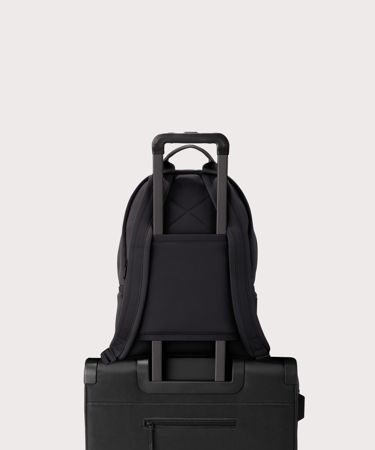 Dagne Dover medium Dakota Neoprene Backpack in onyx strapped to luggage with the neoprene luggage-handle sleeve