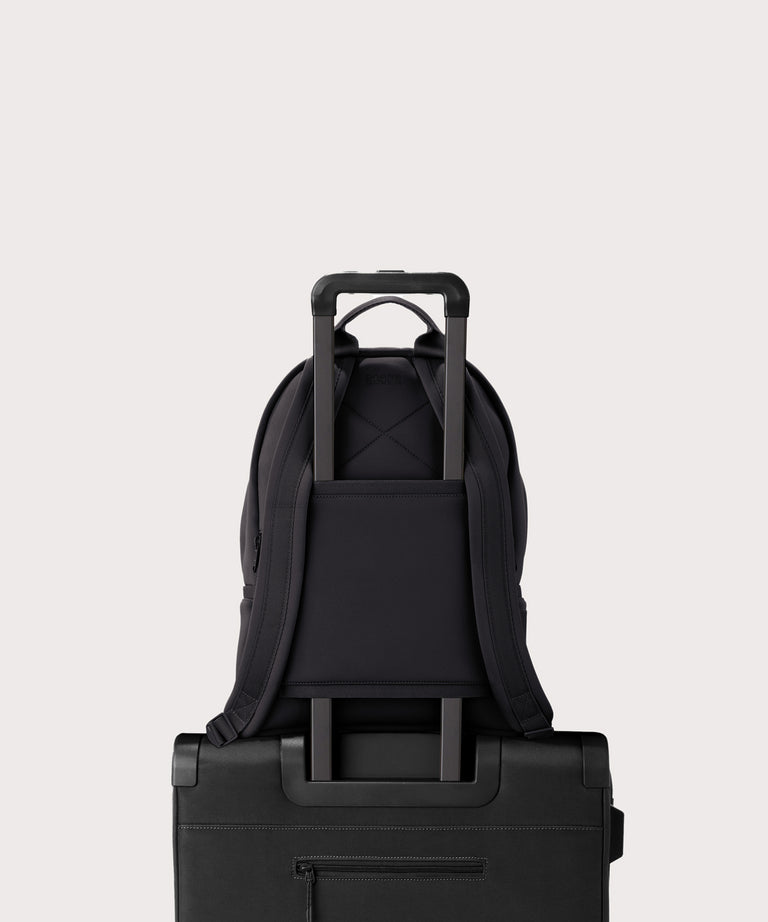 Dagne Dover medium Dakota Neoprene Backpack in onyx strapped to luggage with the neoprene luggage-handle sleeve
