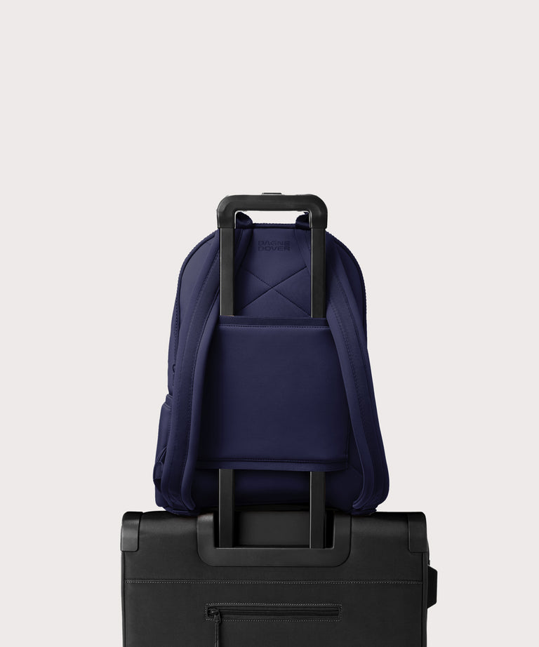 Dagne Dover large Dakota Neoprene Backpack in dark blue strapped to luggage with the neoprene luggage-handle sleeve.
