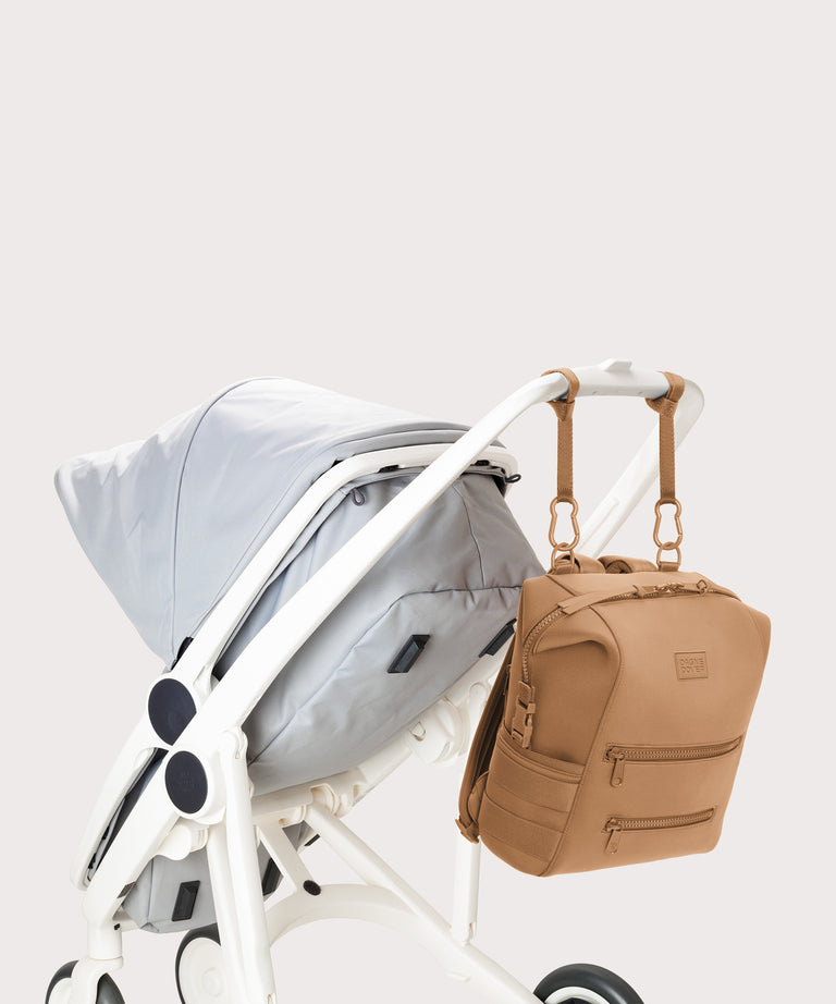 Dagne Dover Medium Indi Diaper Backpack in camel brown attached to a stroller.
