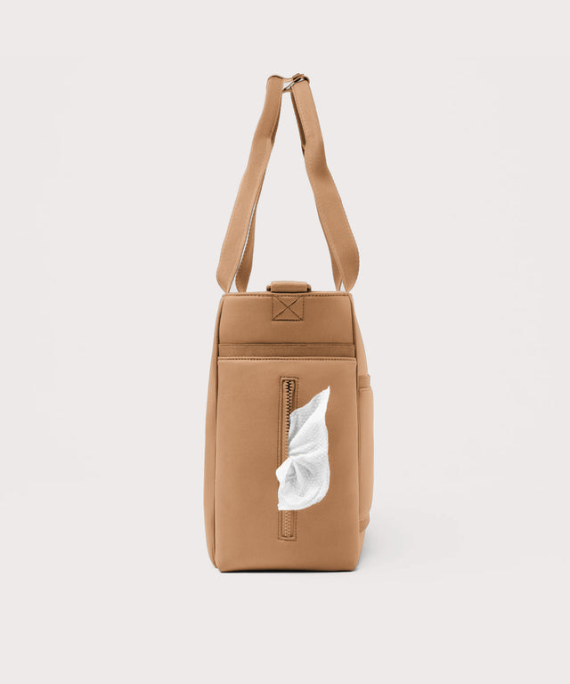 Dagne Dover large Wade Diaper Tote in camel brown seen from the side, with a wet wipe poking out of the slip pocket.
