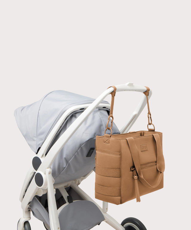 Dagne Dover large Wade Diaper Tote in camel brown strapped to the handle of a stroller.
