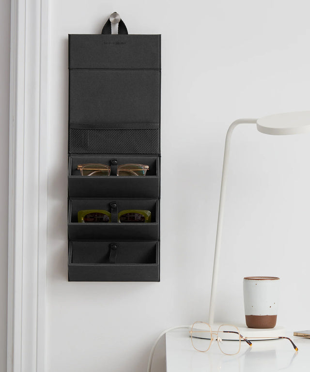 Dagne Dover Remi foldable glasses holder in matcha green hung up and holding glasses by a desk.
