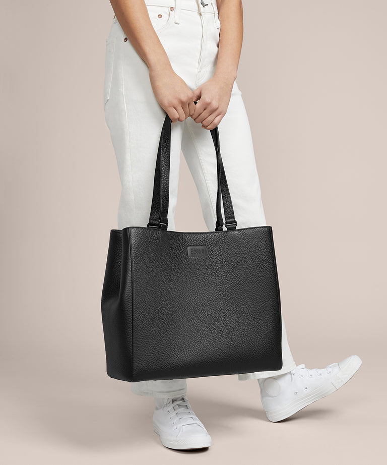 A model holding the 11.25 inch handle of the medium Allyn Tote in black. 