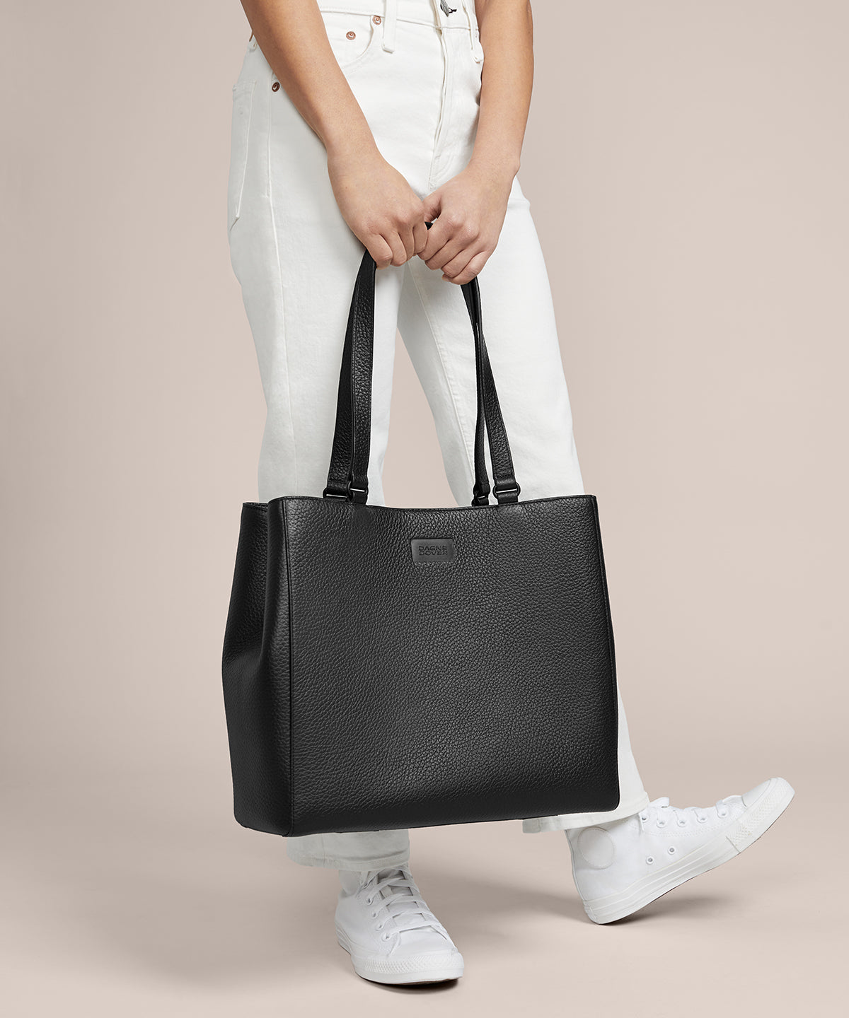 A model holding the 11.25 inch handle of the medium Allyn Tote in black. 