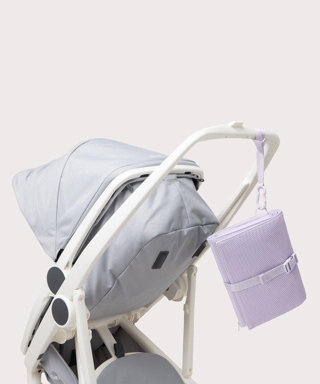 Dagne Dover Joey Changing Kit in  a soft purple with grey undertones strapped to the handle of a stroller.

