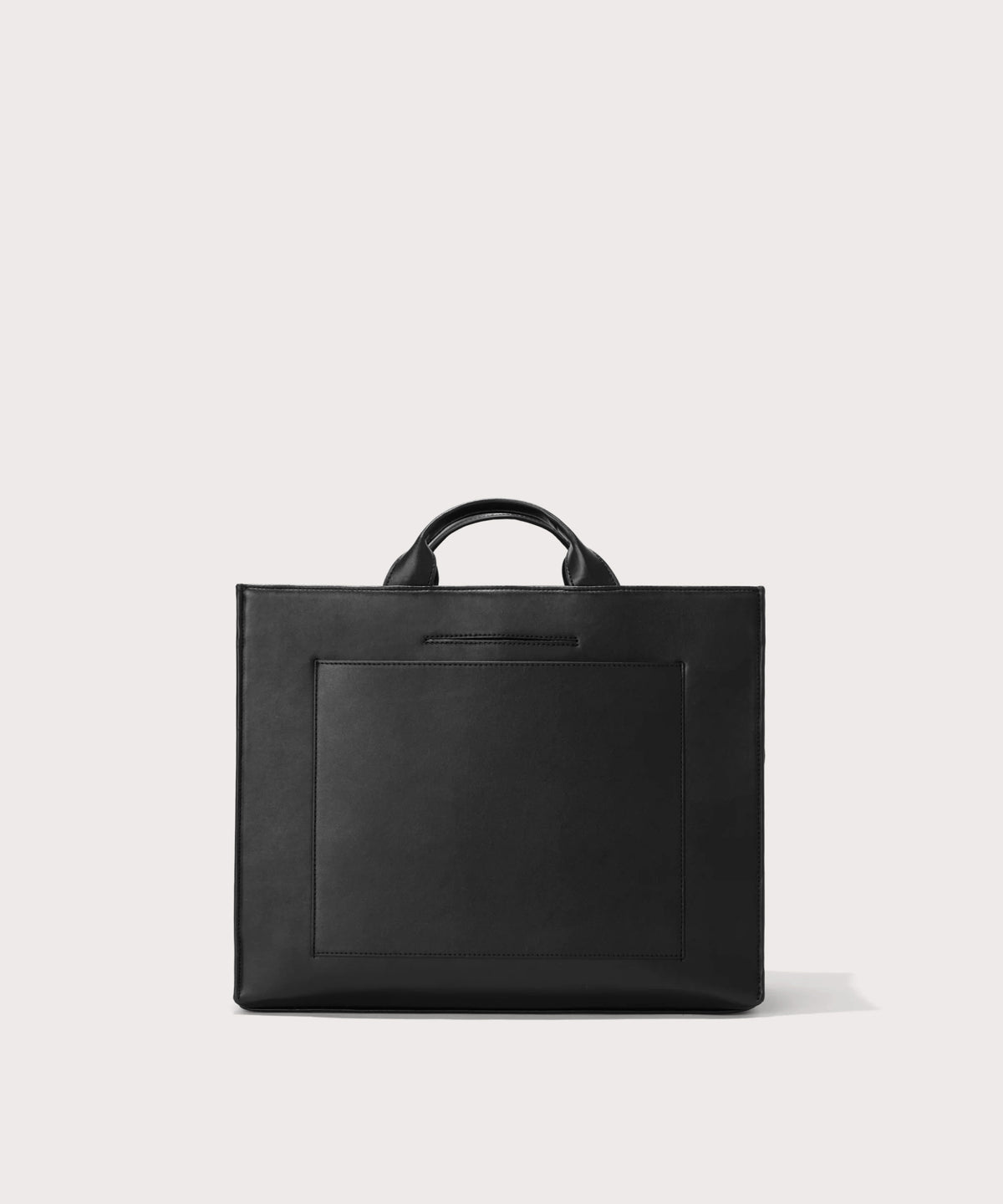 Dagne Dover medium vegan Daily Tote in black revealing the exterior phone pocket and exterior luggage sleeve.

