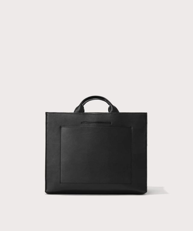 Dagne Dover medium vegan Daily Tote in black revealing the exterior phone pocket and exterior luggage sleeve.
