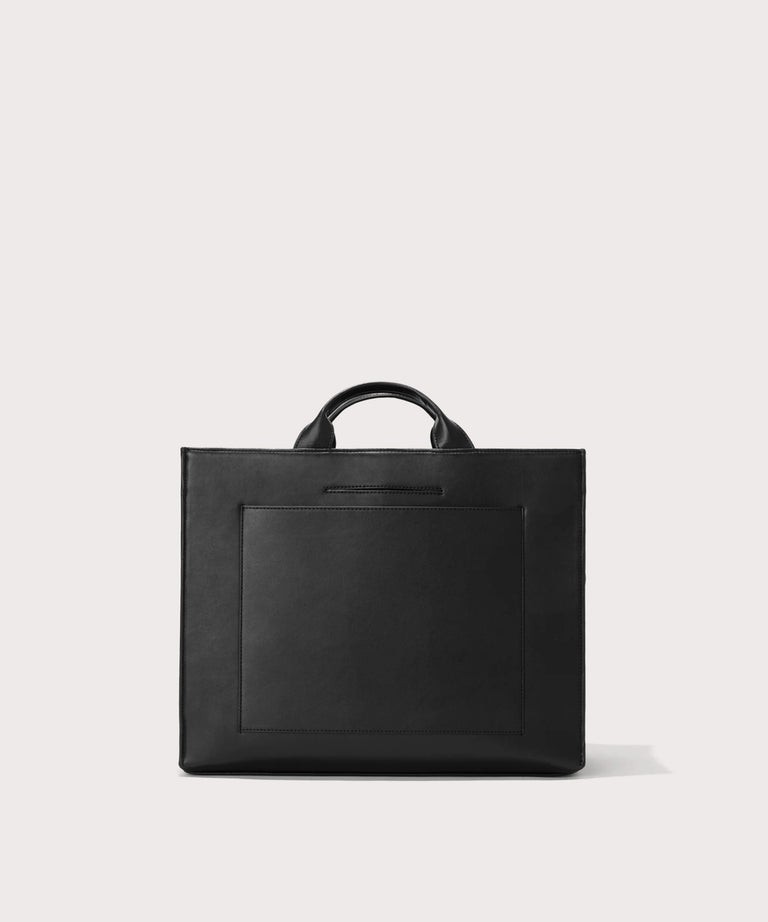 Dagne Dover medium vegan Daily Tote in black revealing the exterior phone pocket and exterior luggage sleeve.
