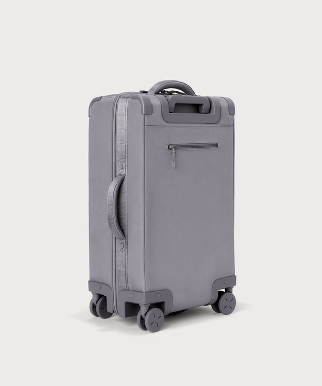 3/4 back view of Seattle carry-on rolling luggage 23.5” in light grey showing side handle and back zippered phone/passport pocket
