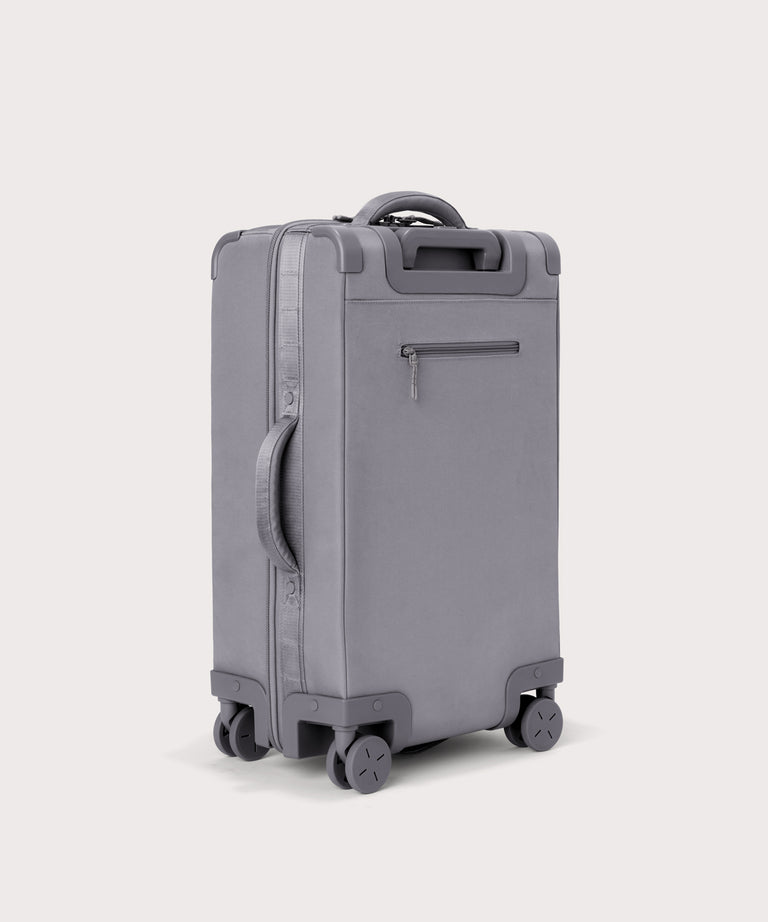 3/4 back view of Seattle carry-on rolling luggage 23.5” in light grey showing side handle and back zippered phone/passport pocket
