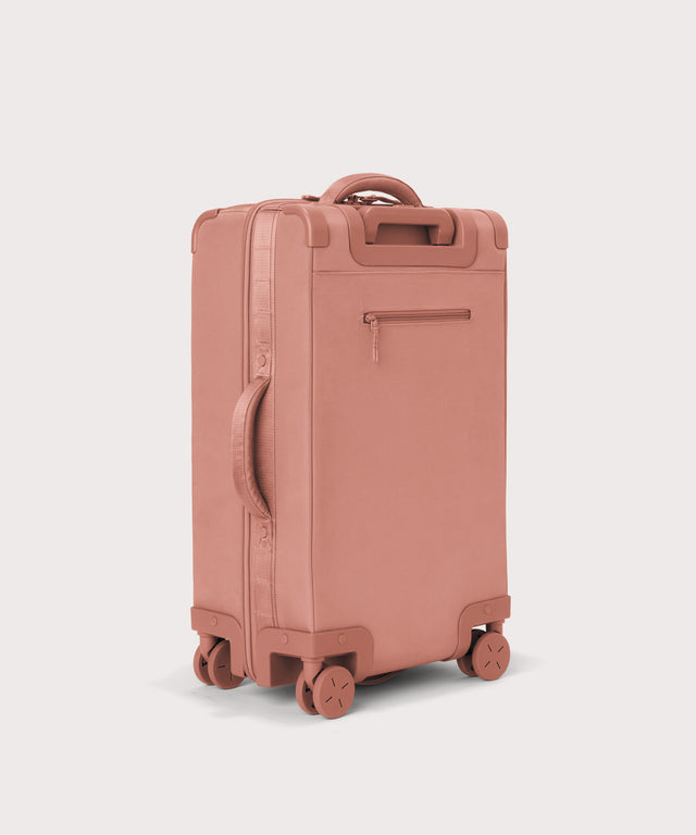 3/4 back view of Seattle carry-on rolling luggage 23.5” in warm dust pink showing side handle and back zippered phone/passport pocket

