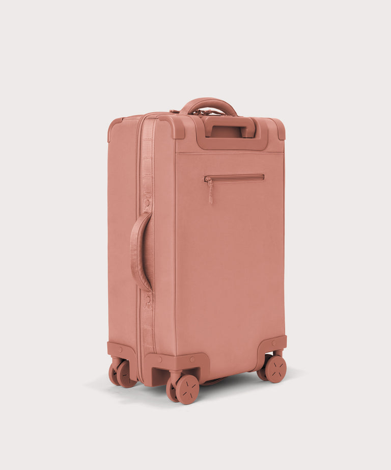 3/4 back view of Seattle carry-on rolling luggage 23.5” in warm dust pink showing side handle and back zippered phone/passport pocket
