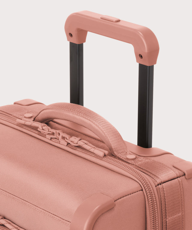 Detail shot of Seattle carry-on rolling luggage 20.5” in warm dust pink extended luggage handle and puffy handle
