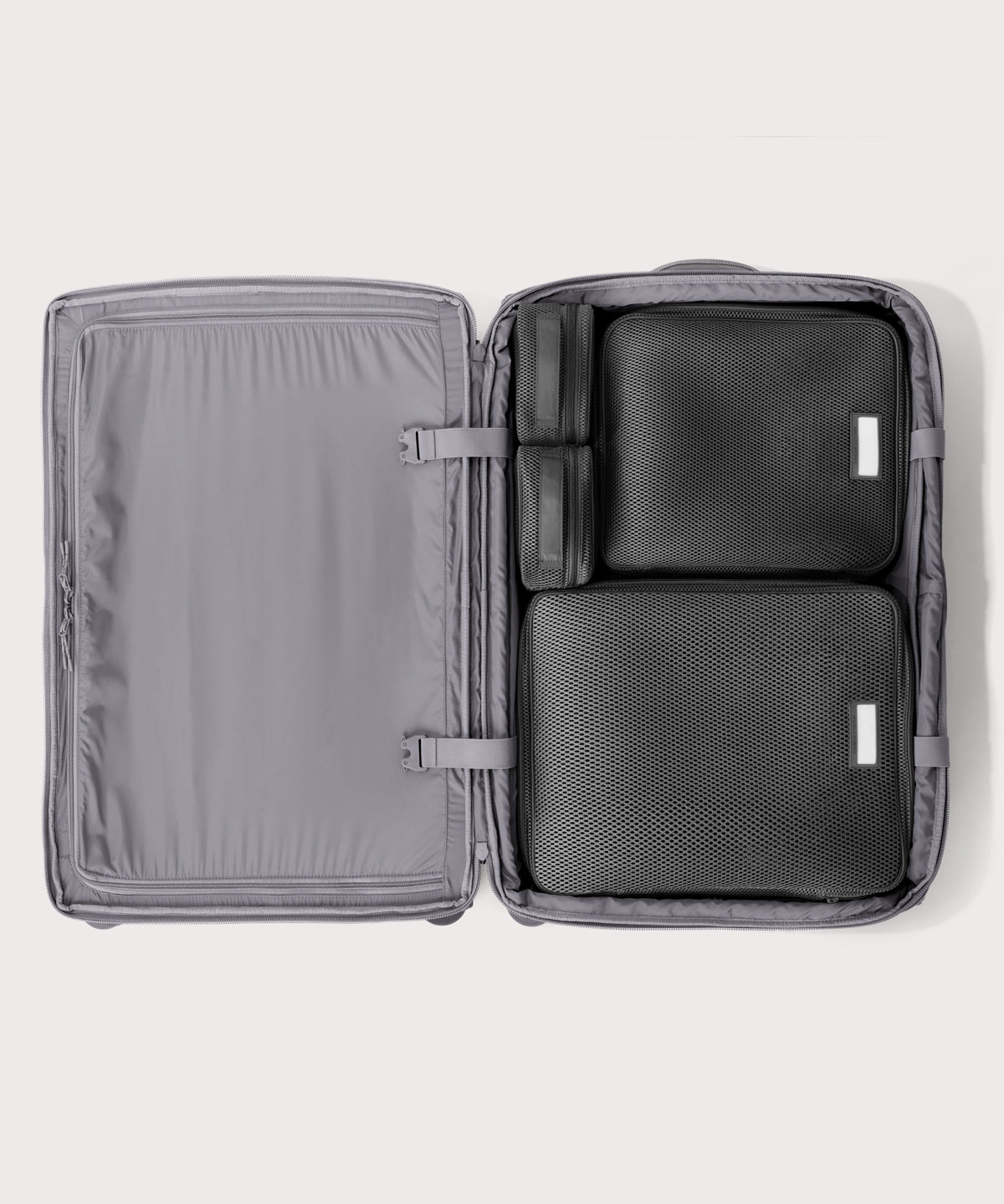 Top down of Sydney checked rolling luggage 28.5” in light grey with interior divider zipped and packing cubes packed into the right side. 
