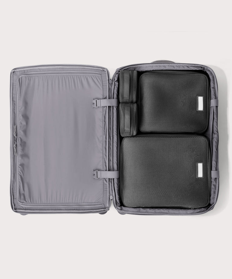 Top down of Sydney checked rolling luggage 28.5” in light grey with interior divider zipped and packing cubes packed into the right side. 
