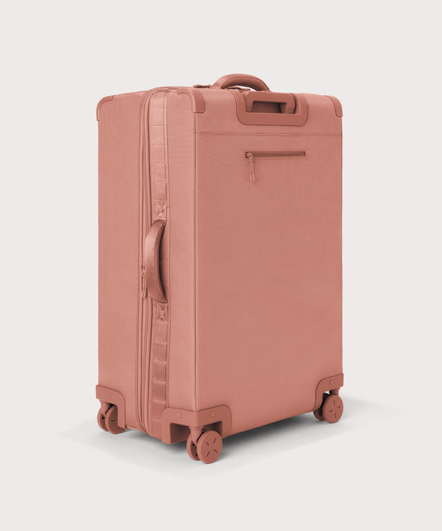 3/4 back view of Sydney checked rolling luggage 28.5” in warm dust pink showing side handle and back zippered phone/passport pocket
