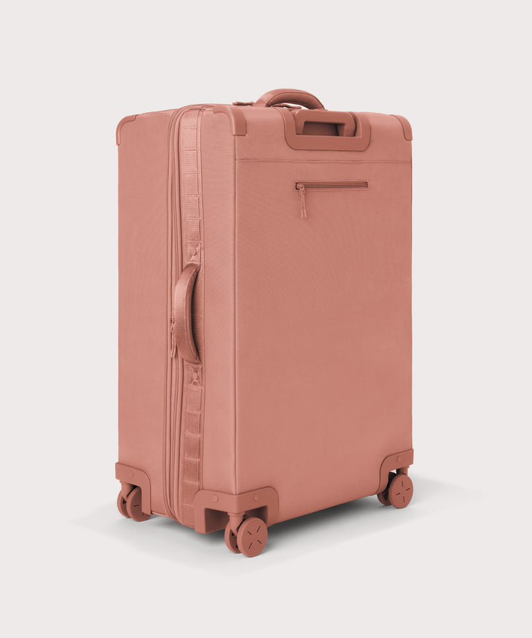 3/4 back view of Sydney checked rolling luggage 28.5” in warm dust pink showing side handle and back zippered phone/passport pocket
