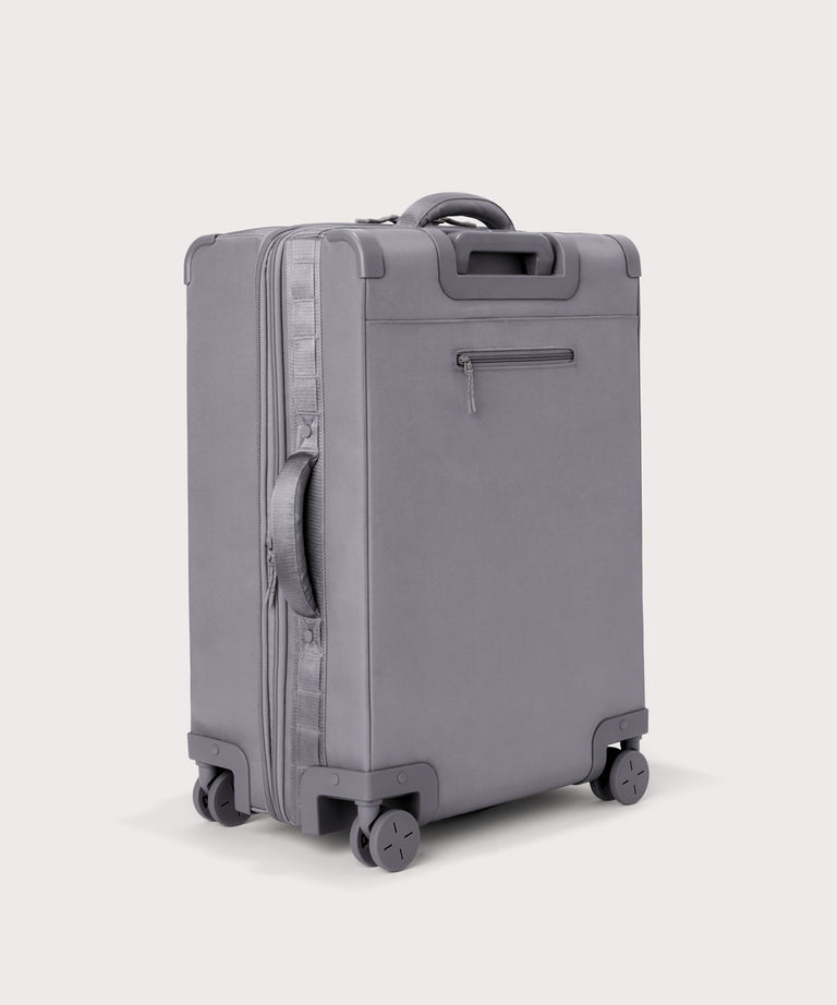 3/4 back view of Sydney checked rolling luggage 25" in light grey showing side handle and back zippered phone/passport pocket
