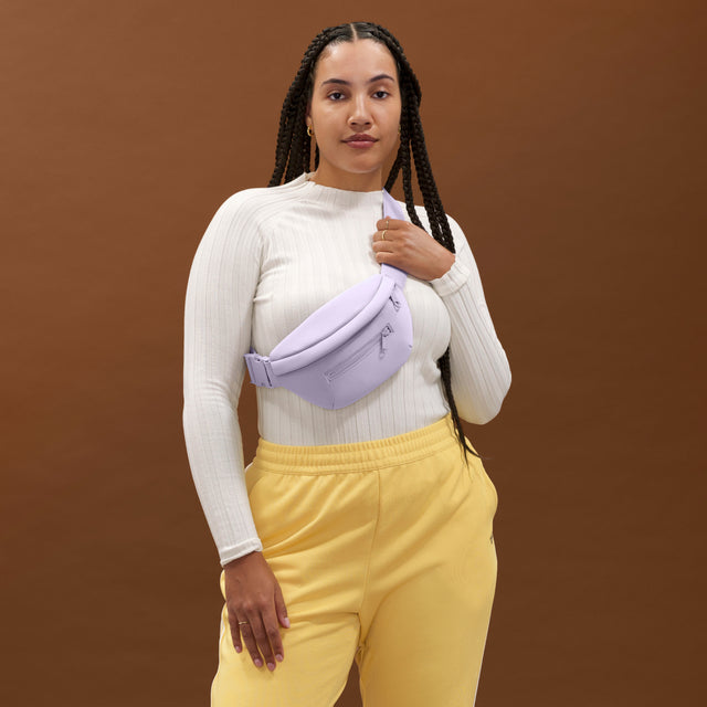 NoPDP A woman wearing the Ace Fanny Pack in light purple as a crossbody bag. Model: Logan is  5'11"