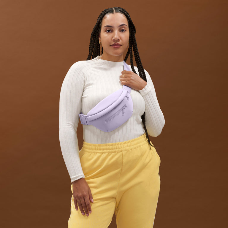 NoPDP A woman wearing the Ace Fanny Pack in light purple as a crossbody bag. Model: Logan is  5'11"